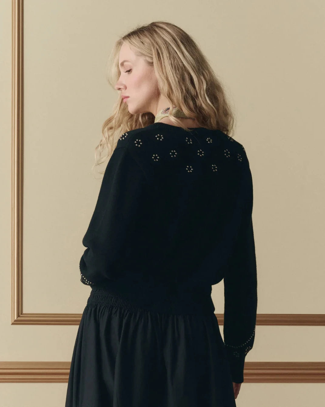 Woman wearing a black dress with decorative elements on a beige wall background