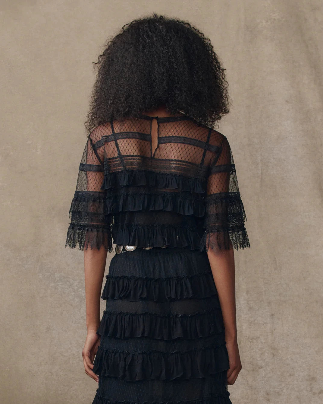 Black ruffled dress worn by a model against a beige background