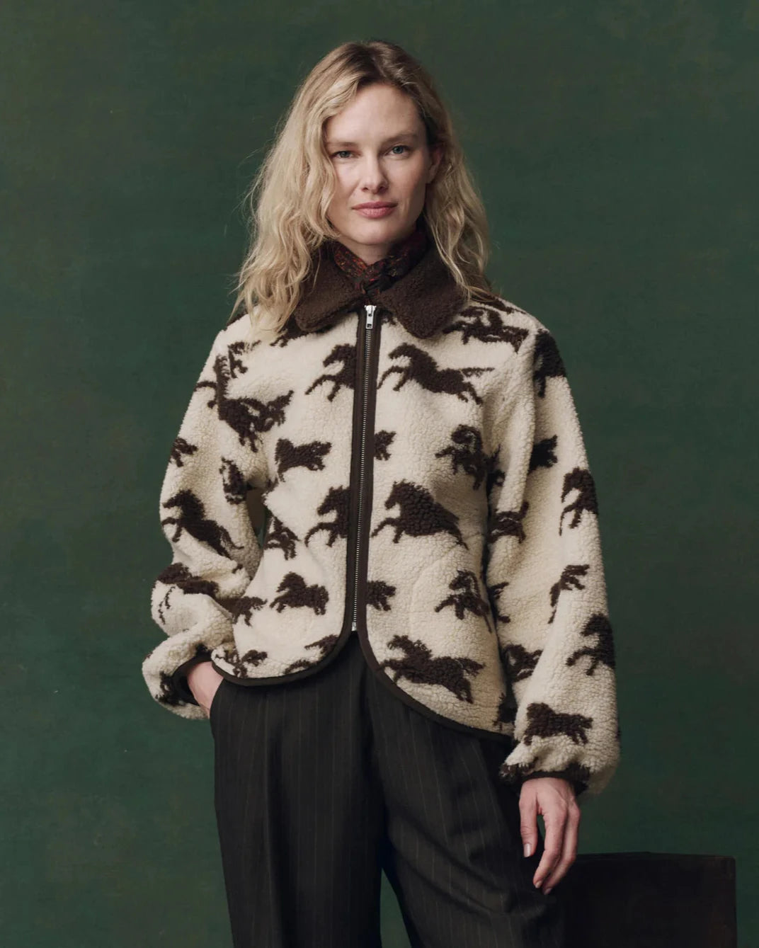 Woman wearing a patterned jacket with horse designs against a green background