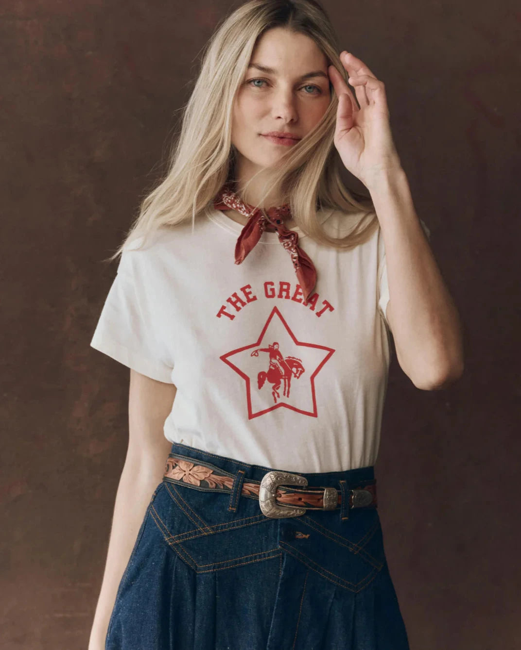 Woman wearing a white t-shirt with a red graphic design and a bandana, standing against a brown background.
