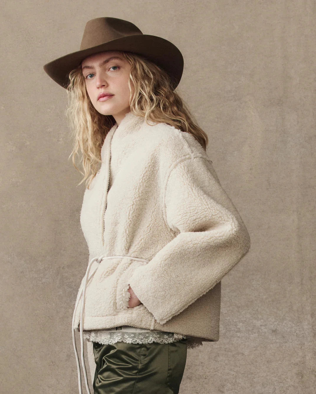 Woman wearing a beige coat and brown hat against a beige background