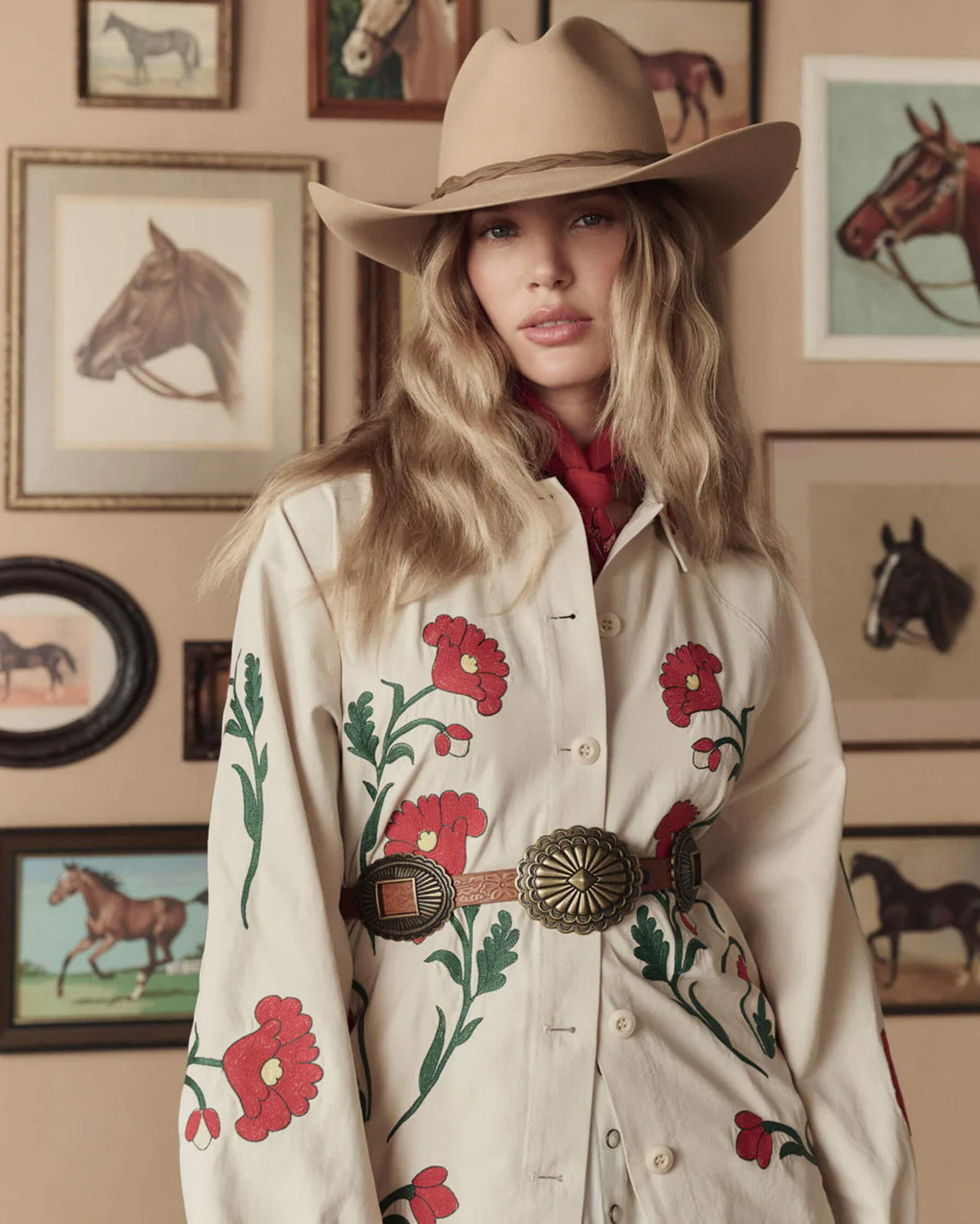 Woman wearing a cowboy hat and floral embroidered shirt in a room with horse-themed decor.