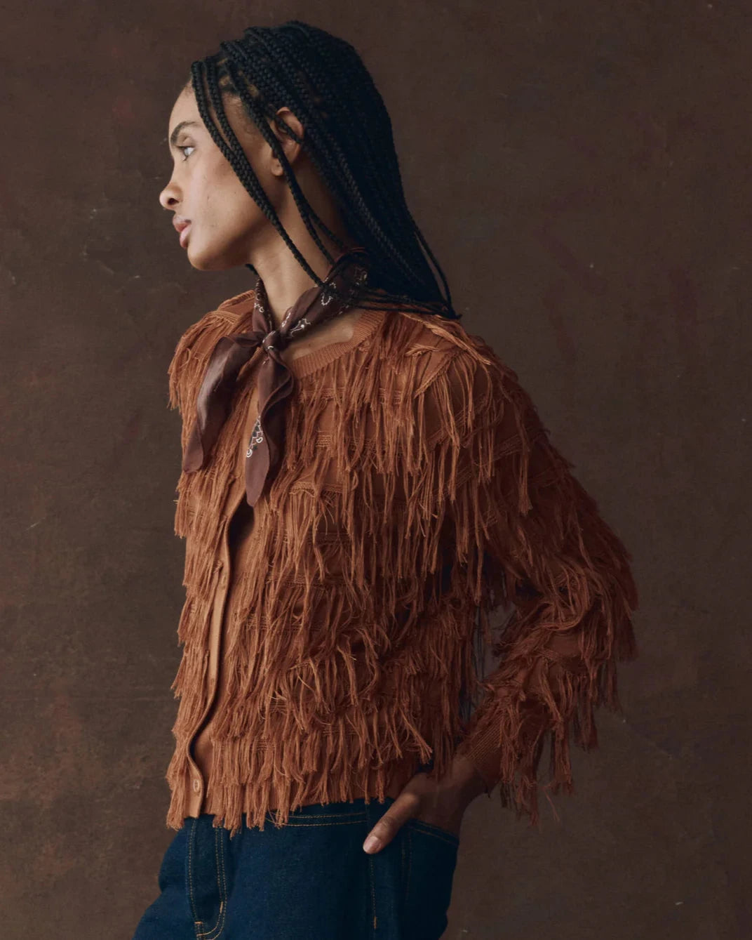 Woman wearing a brown fringed jacket against a brown background