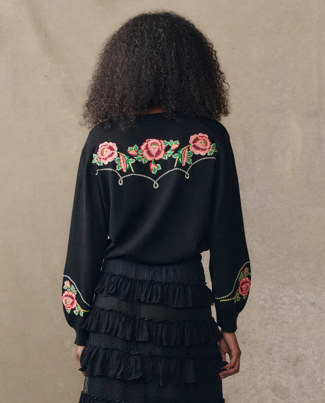 Person wearing a black outfit with floral embroidery on a beige background