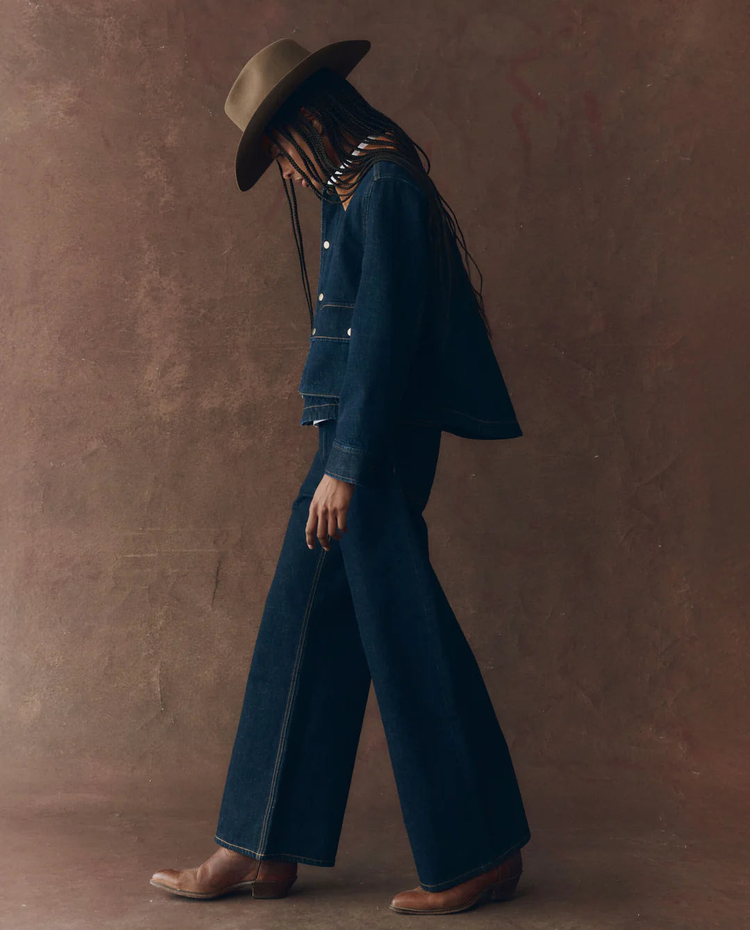 Person wearing a blue outfit and hat against a brown background