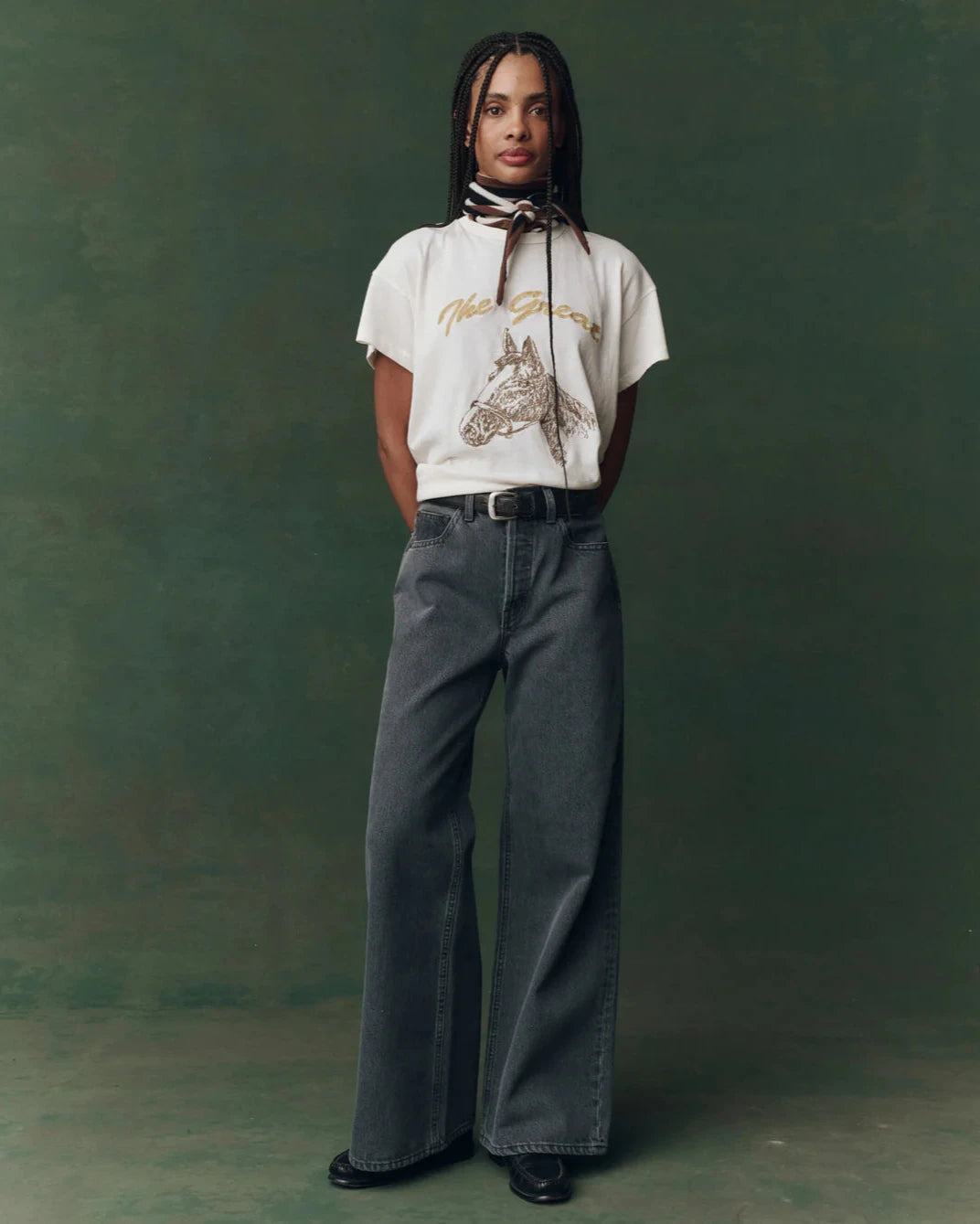 Person wearing a white t-shirt with a graphic design and gray pants against a green background