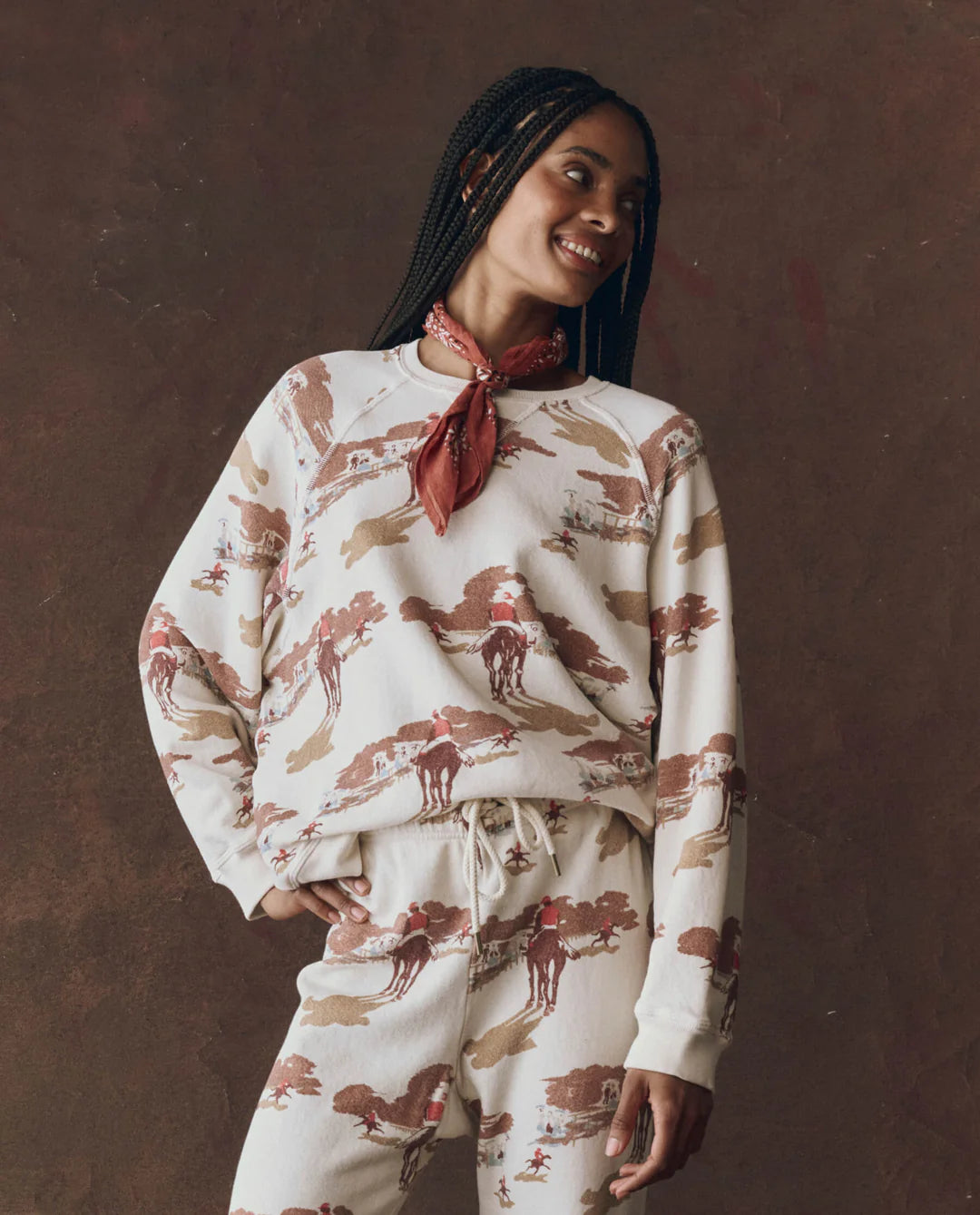 Woman wearing a white sweatshirt and pants with red and brown patterns against a brown background