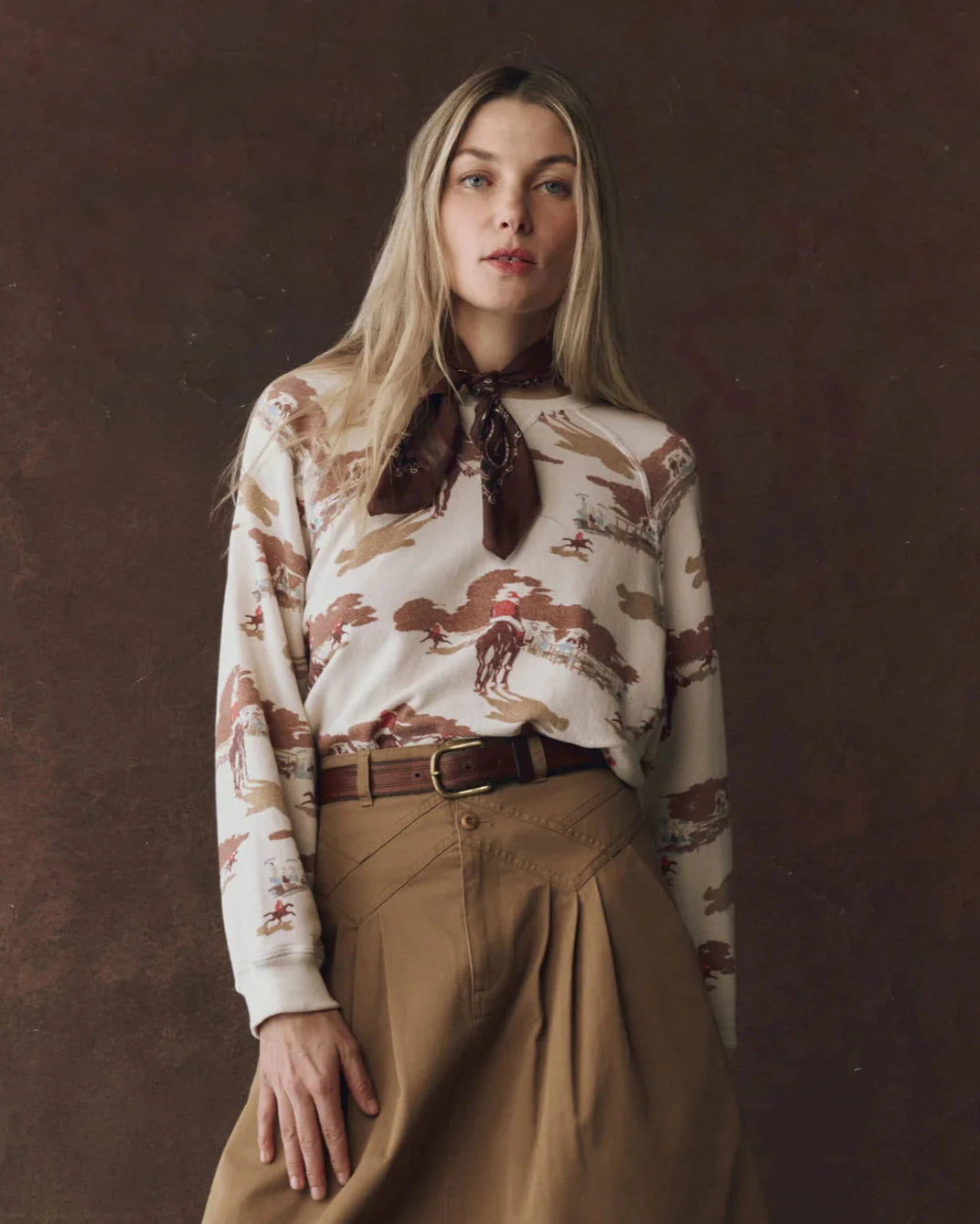 Woman wearing a patterned blouse and beige skirt against a brown background