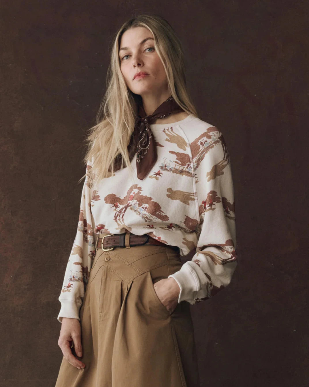 Woman wearing a patterned blouse and brown pants against a dark background