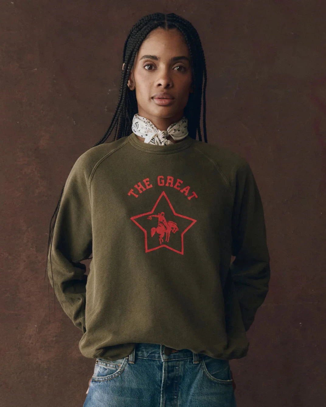 Person wearing a green sweatshirt with 'The Great' logo on a brown background