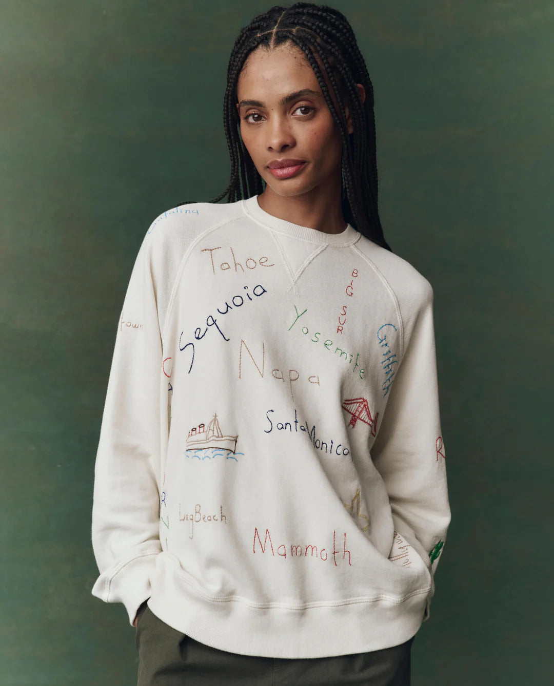 Person wearing a white sweatshirt with embroidered text and graphics on a green background