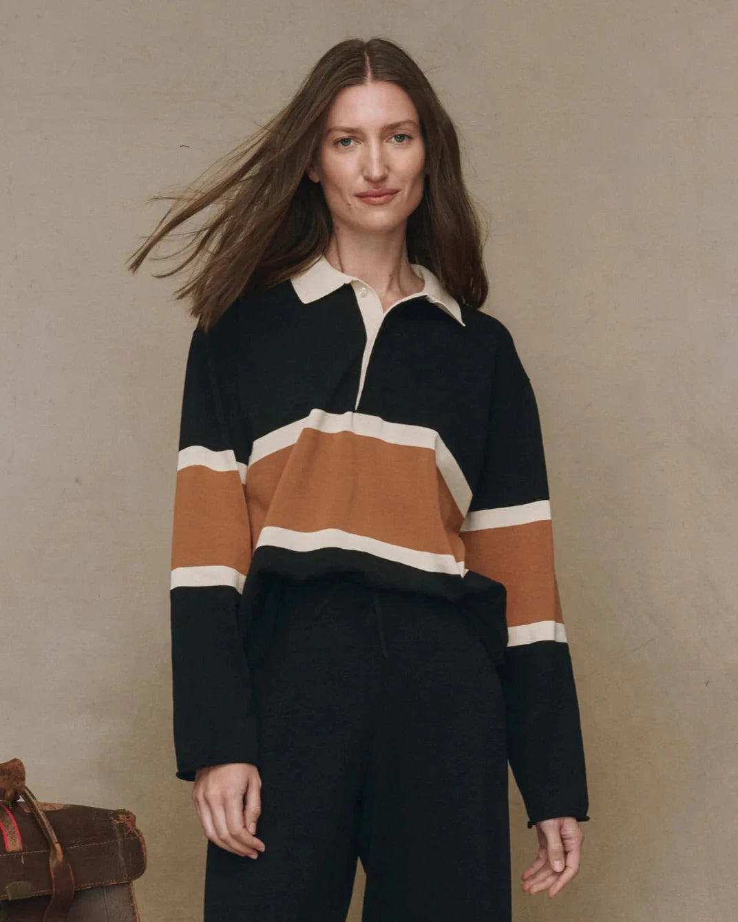 Woman wearing a black, brown, and white striped sweater against a beige background