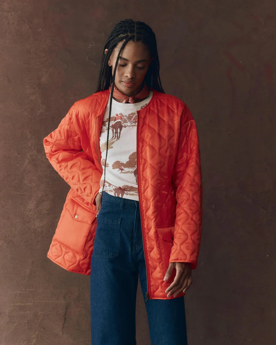 Person wearing an orange quilted jacket over a graphic t-shirt with a brown background