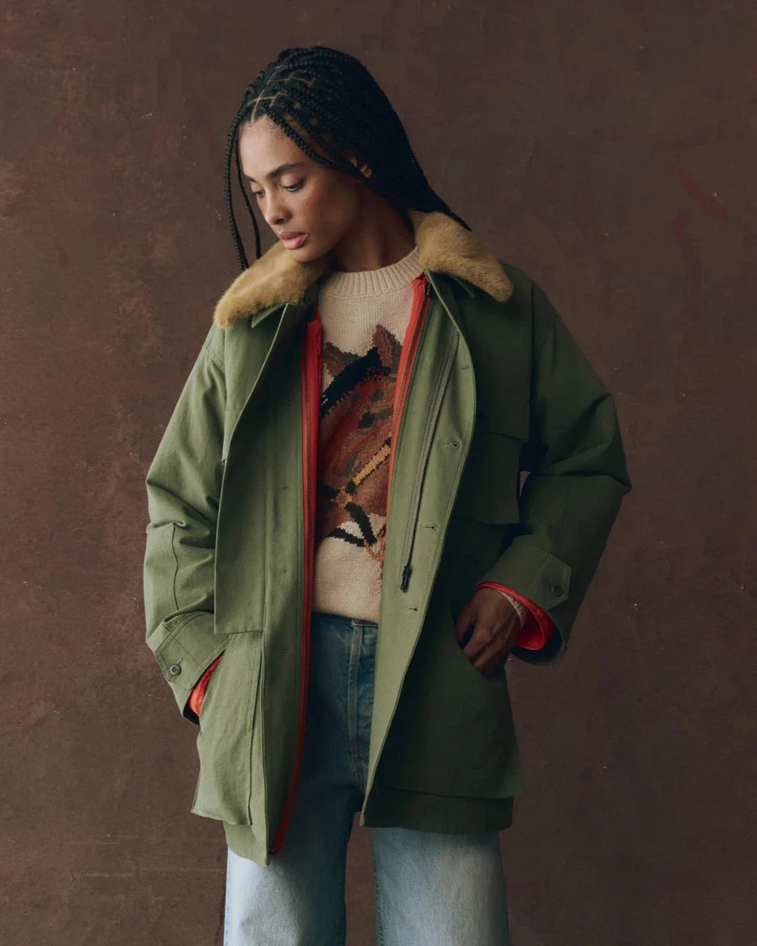 Woman wearing a green coat with fur collar against a brown background