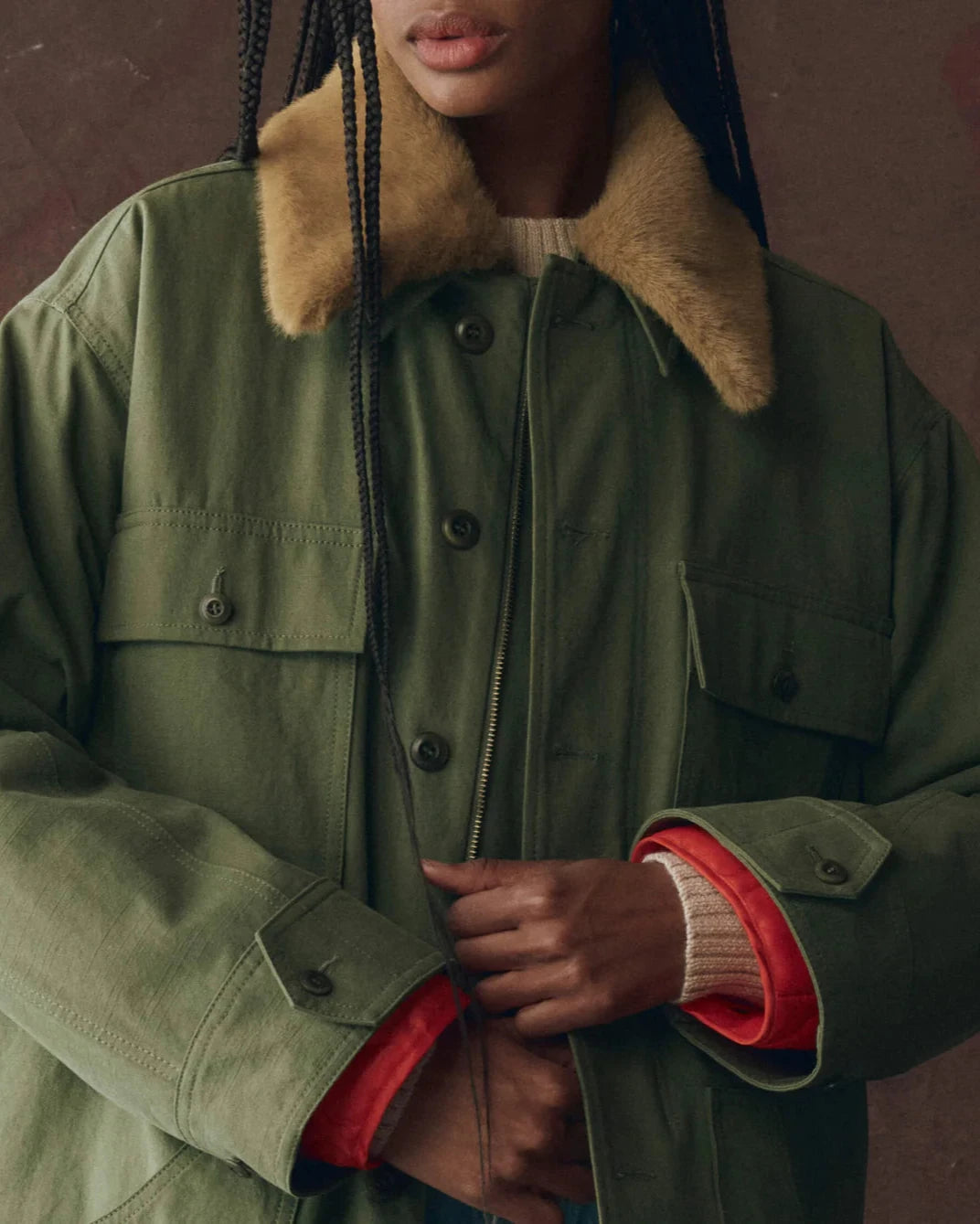Person wearing a green jacket with a fur-lined hood against a dark background