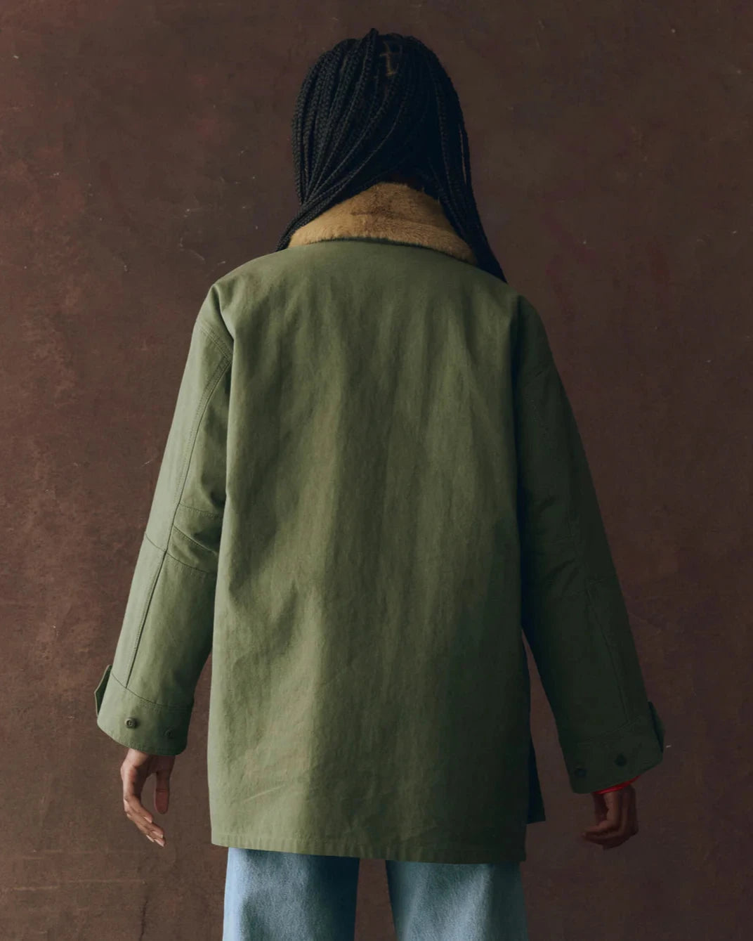 Person wearing a green coat with a hood against a brown background