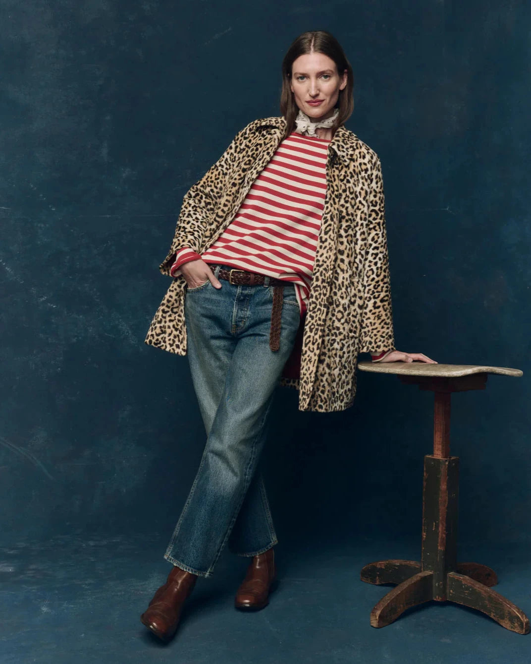 Woman wearing a leopard print coat, striped shirt, and jeans against a blue background