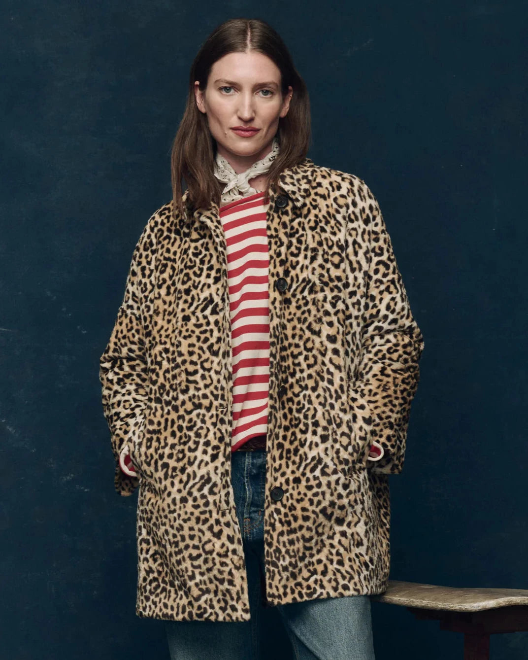 Woman wearing a leopard print coat over a striped shirt against a dark blue background