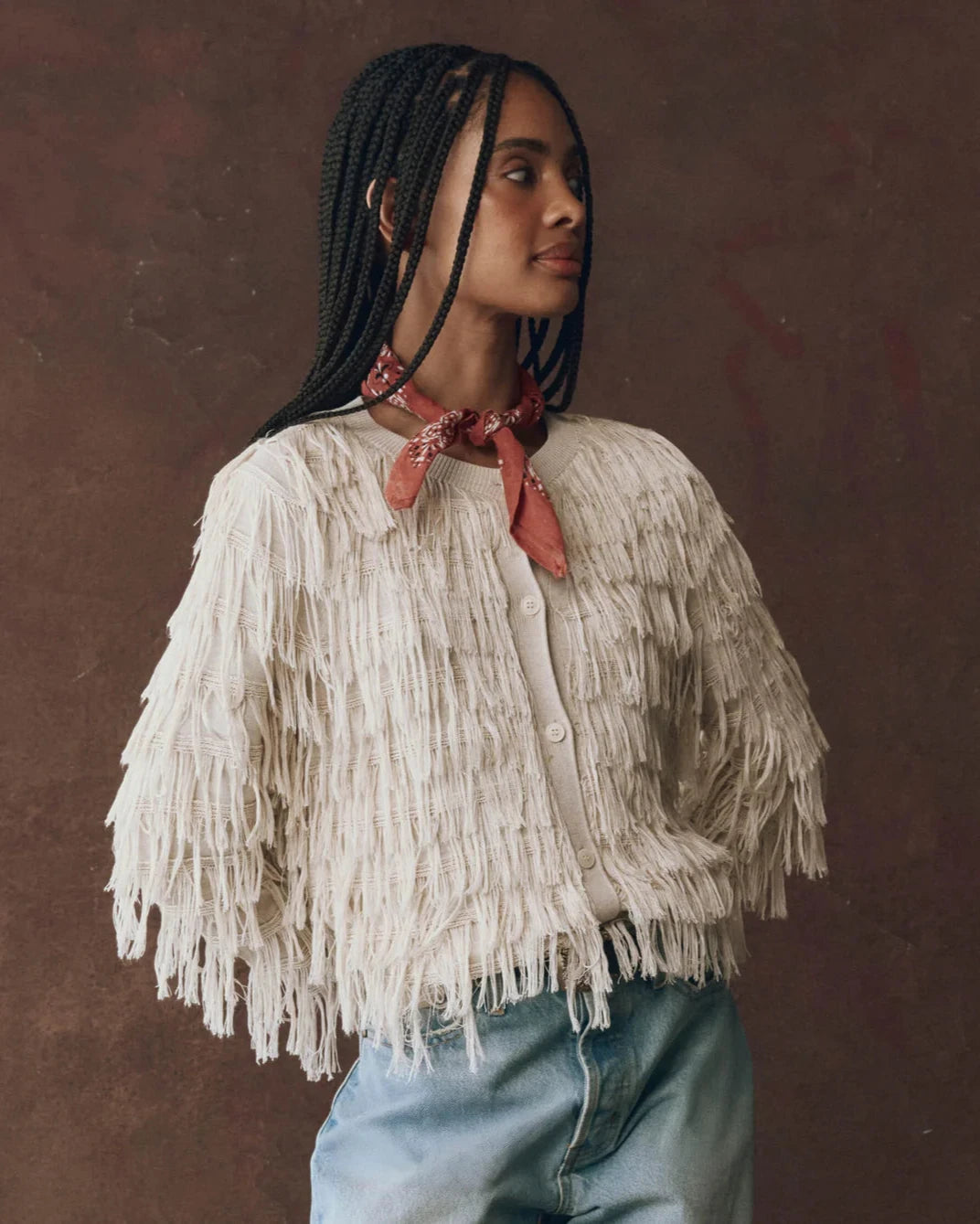 Woman wearing a white fringed sweater and blue jeans with a brown background