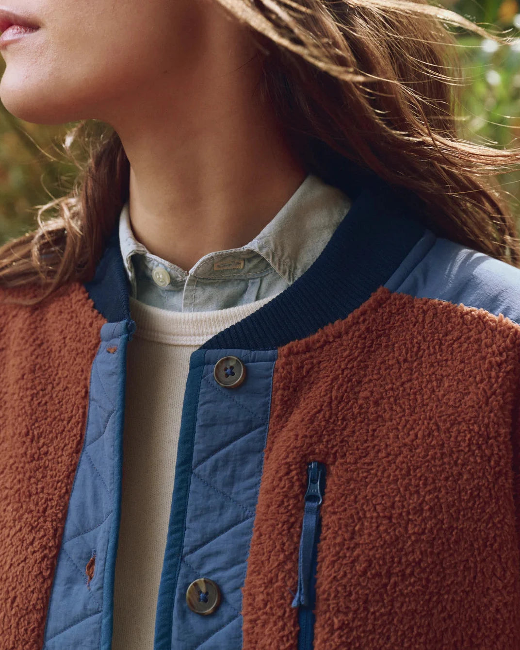 Close-up of a person wearing a brown and blue jacket with a blurred natural background