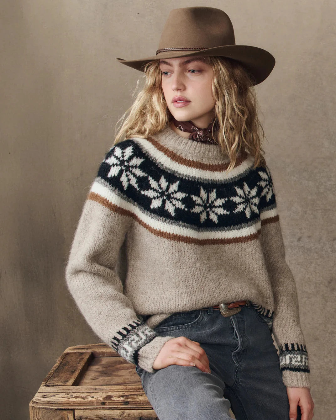 Woman wearing a patterned sweater and brown hat against a neutral background