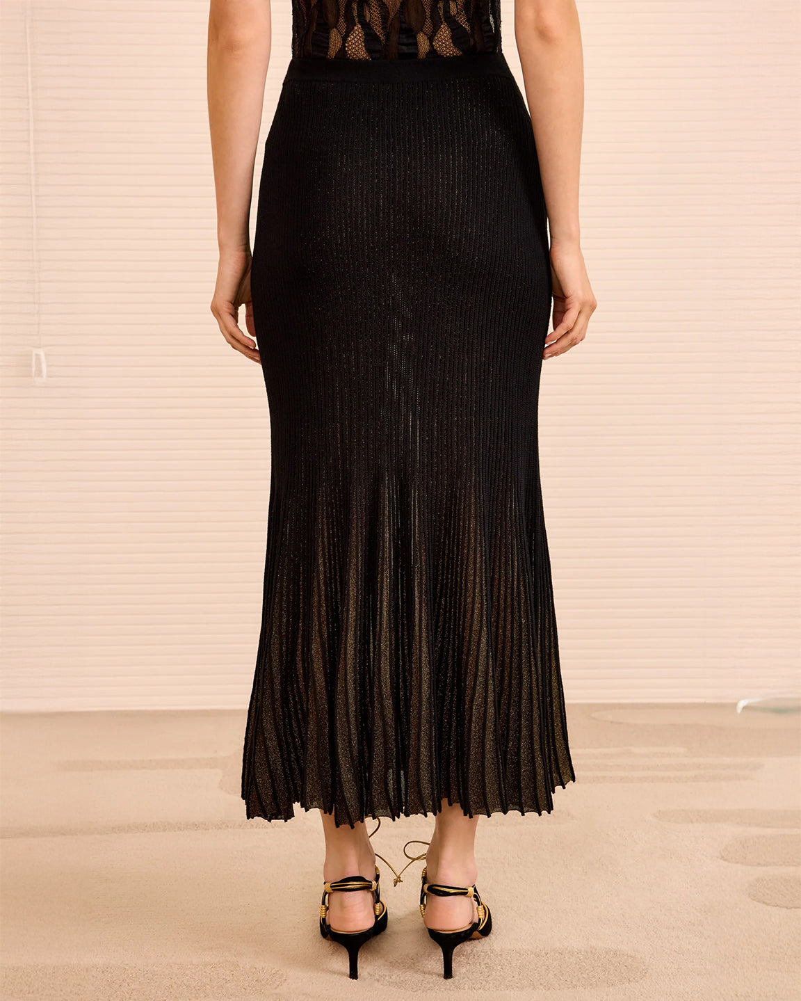 Person wearing a black pleated skirt with a plain background