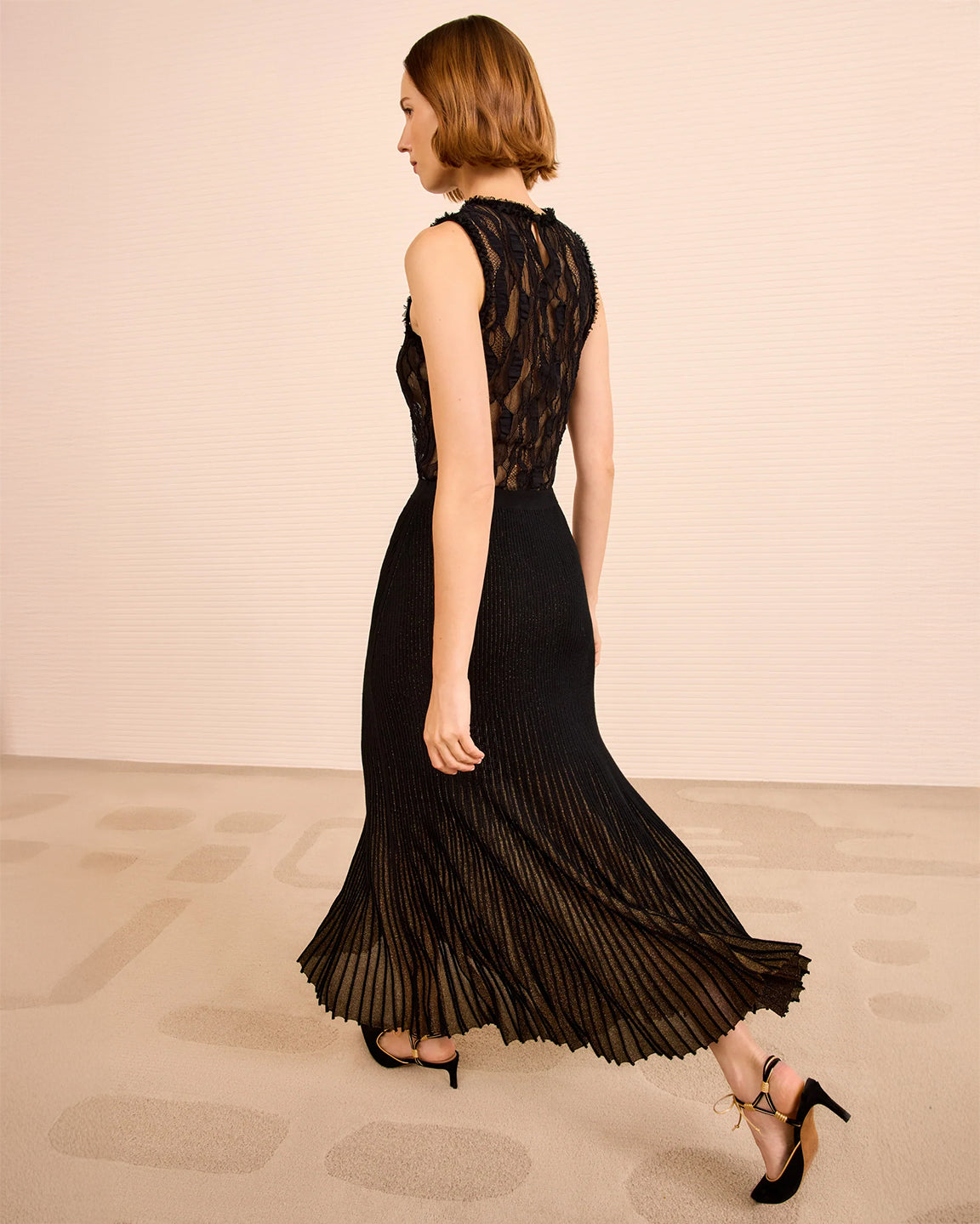 Woman wearing a black pleated skirt with sheer lace top on a beige background