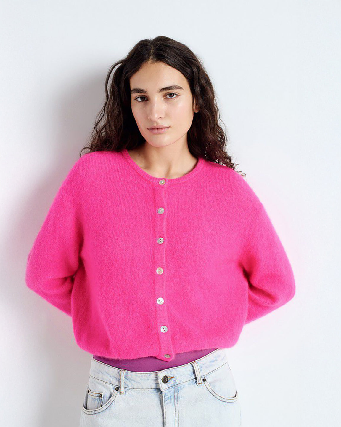 Woman wearing a bright pink cardigan against a white background