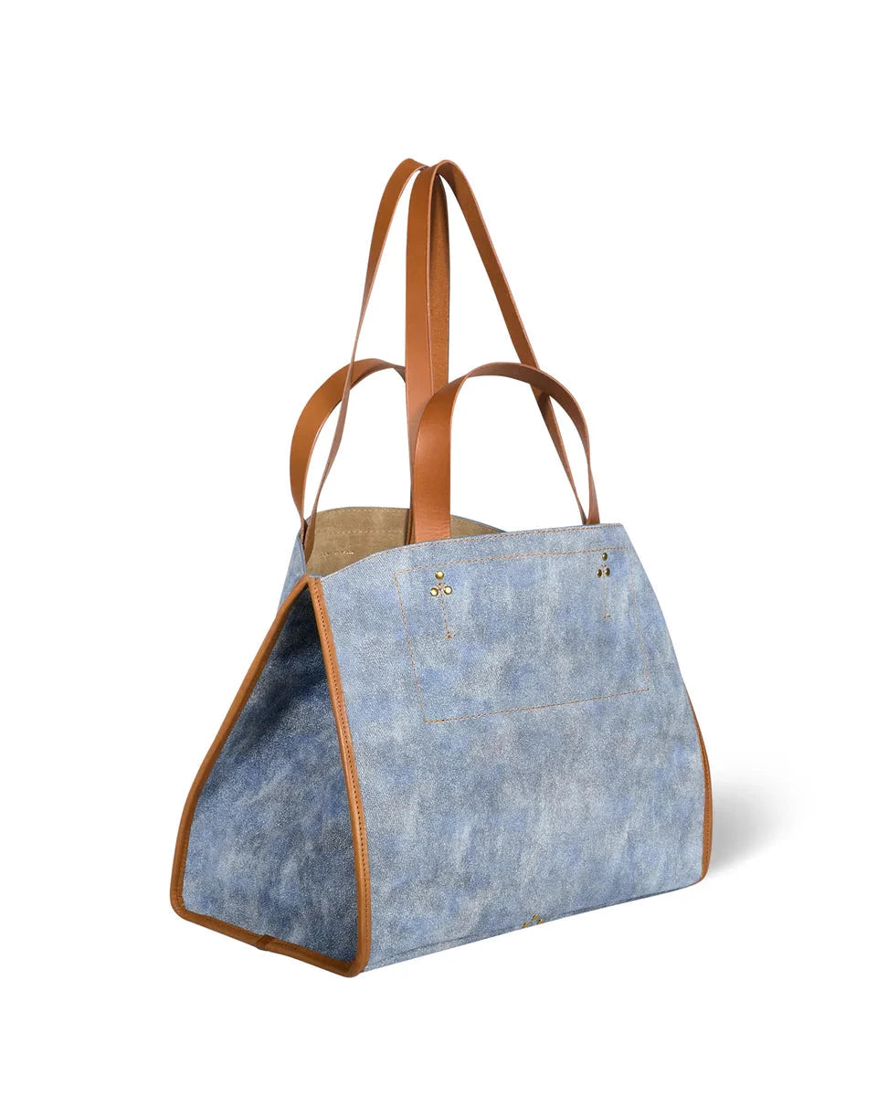 Blue denim tote bag with brown leather handles on a white background