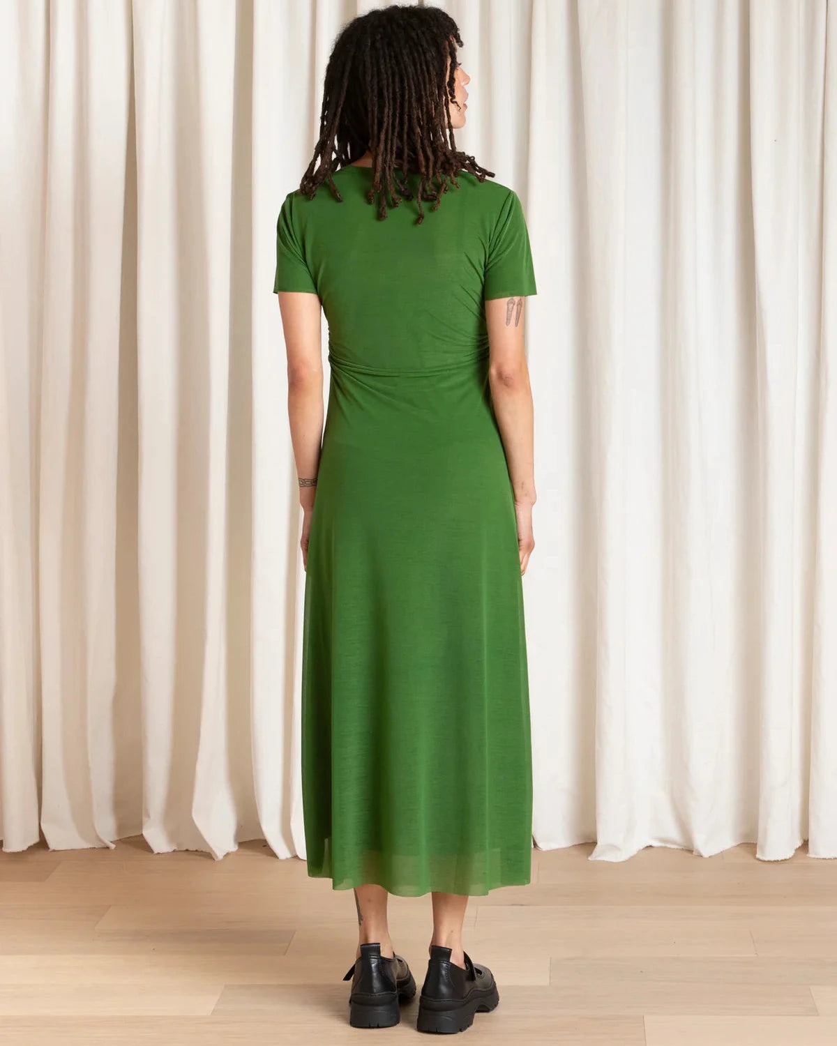 Person wearing a green dress standing in front of white curtains