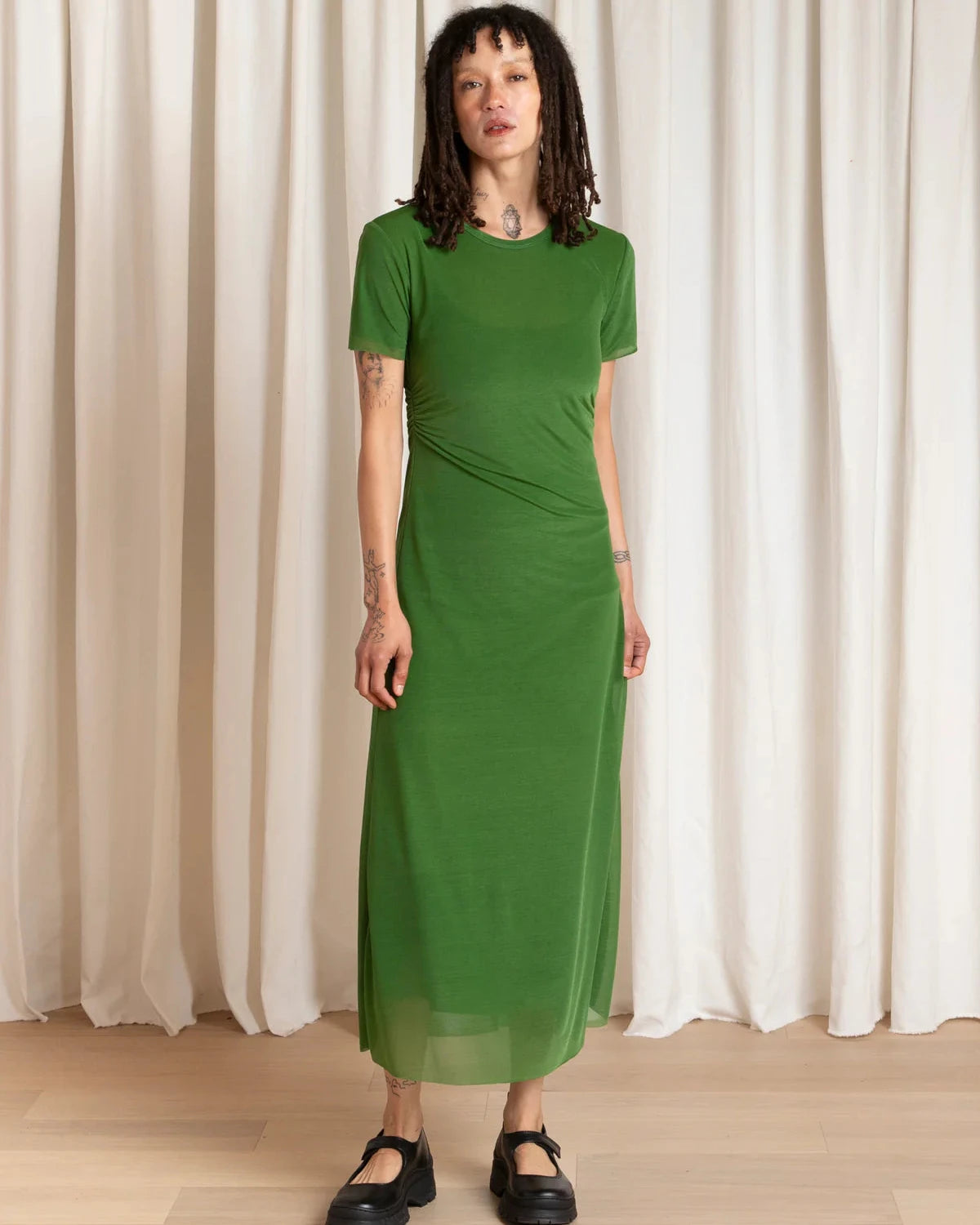 Woman wearing a green dress standing against a white curtain