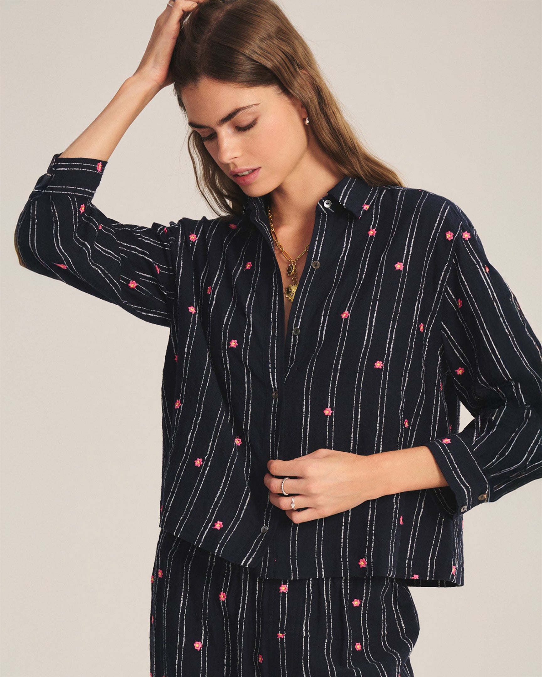 Woman wearing a navy blue pajama set with pink floral patterns on a plain background