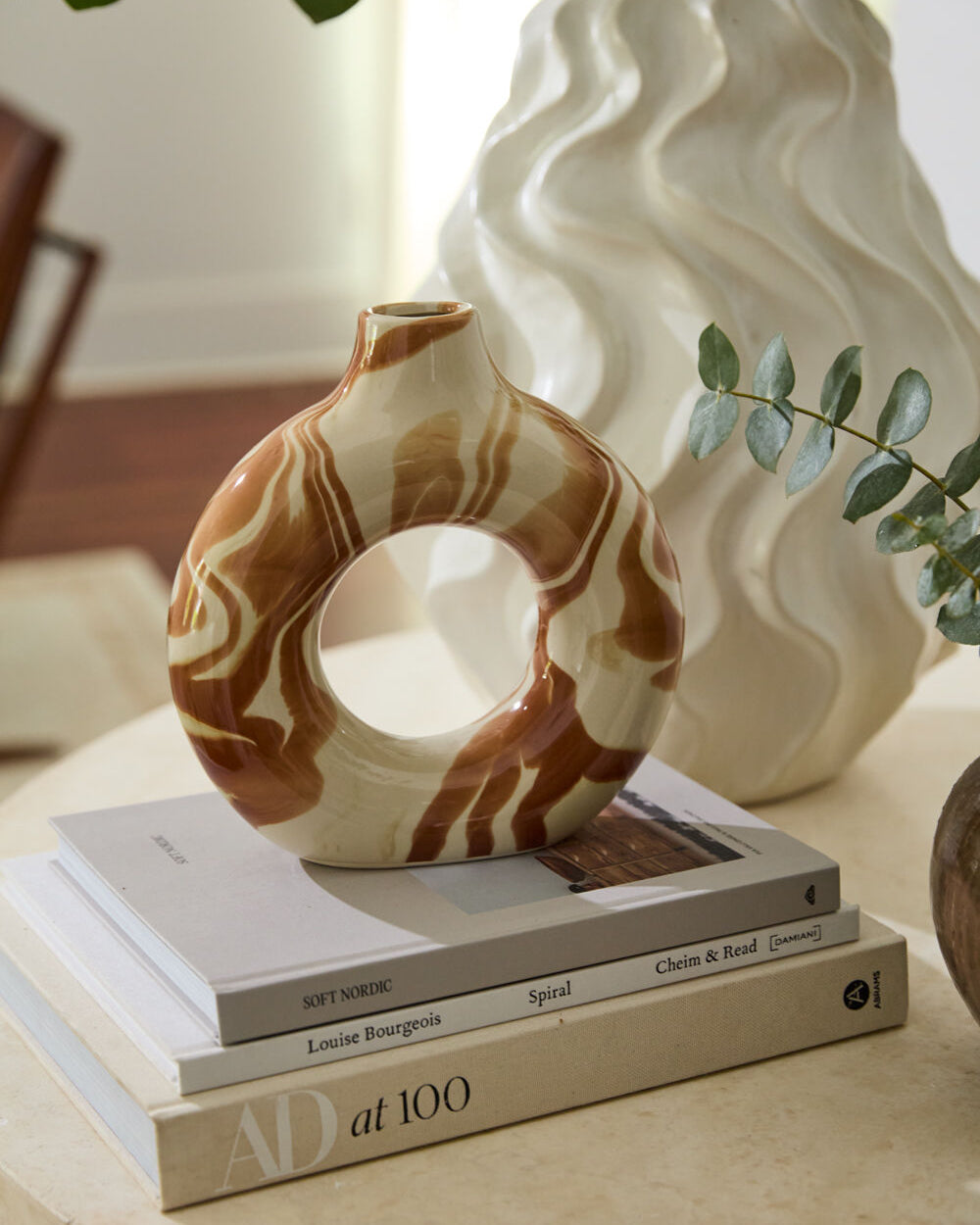 Decorative ceramic vase on books with a wavy-patterned vase in the background