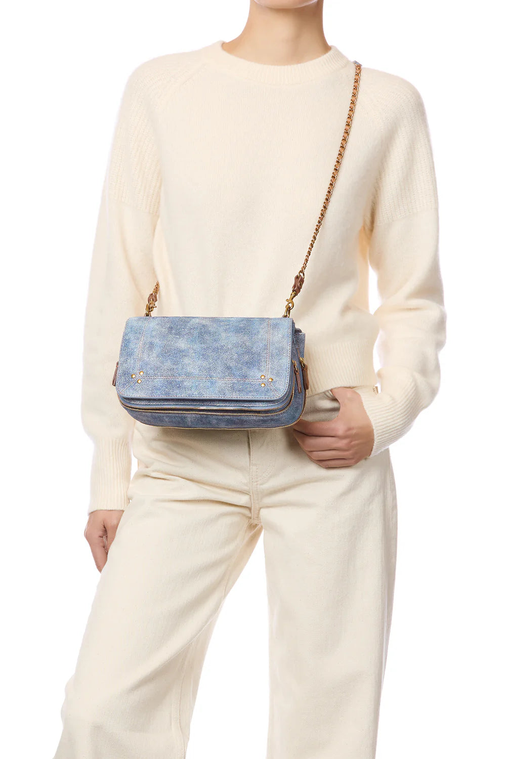 Person wearing a cream sweater and pants with a blue handbag featuring gold chain strap.