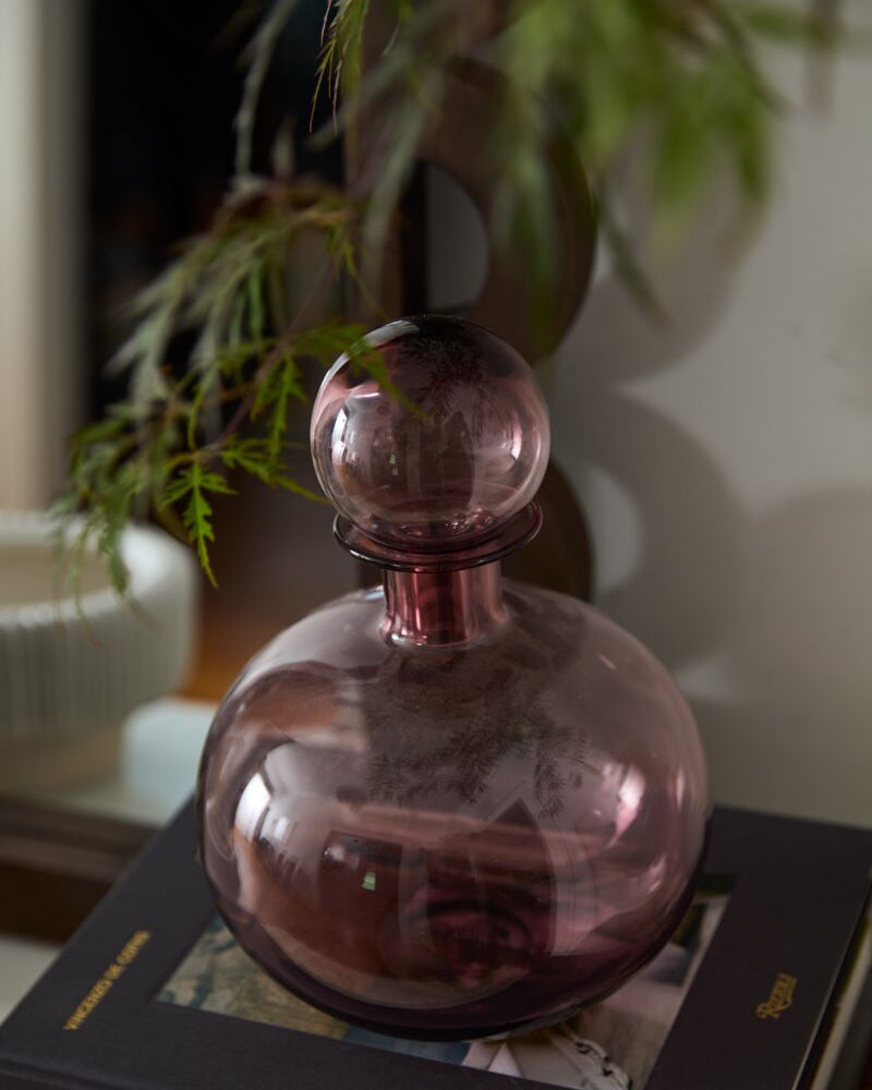 Pink glass bottle on a book with a blurred plant in the background