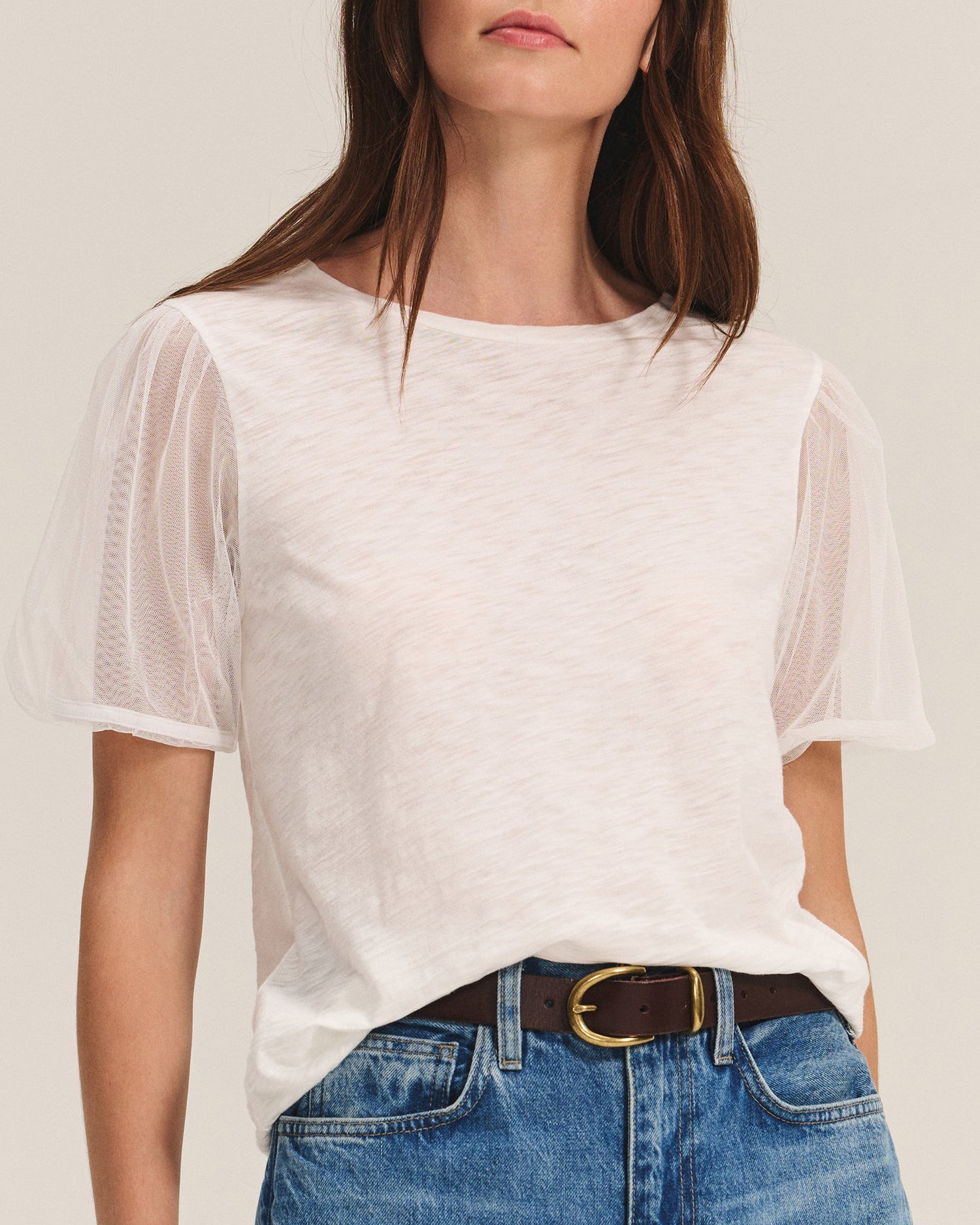 Woman wearing a white sheer top and blue jeans on a plain background