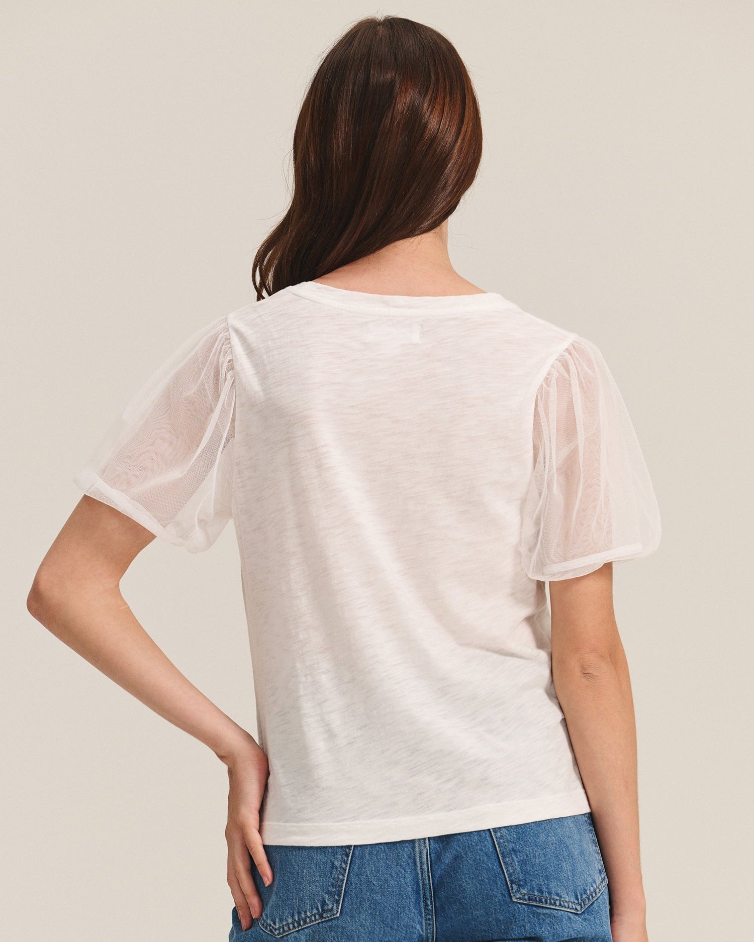 Woman wearing a white sheer top and blue jeans on a beige background