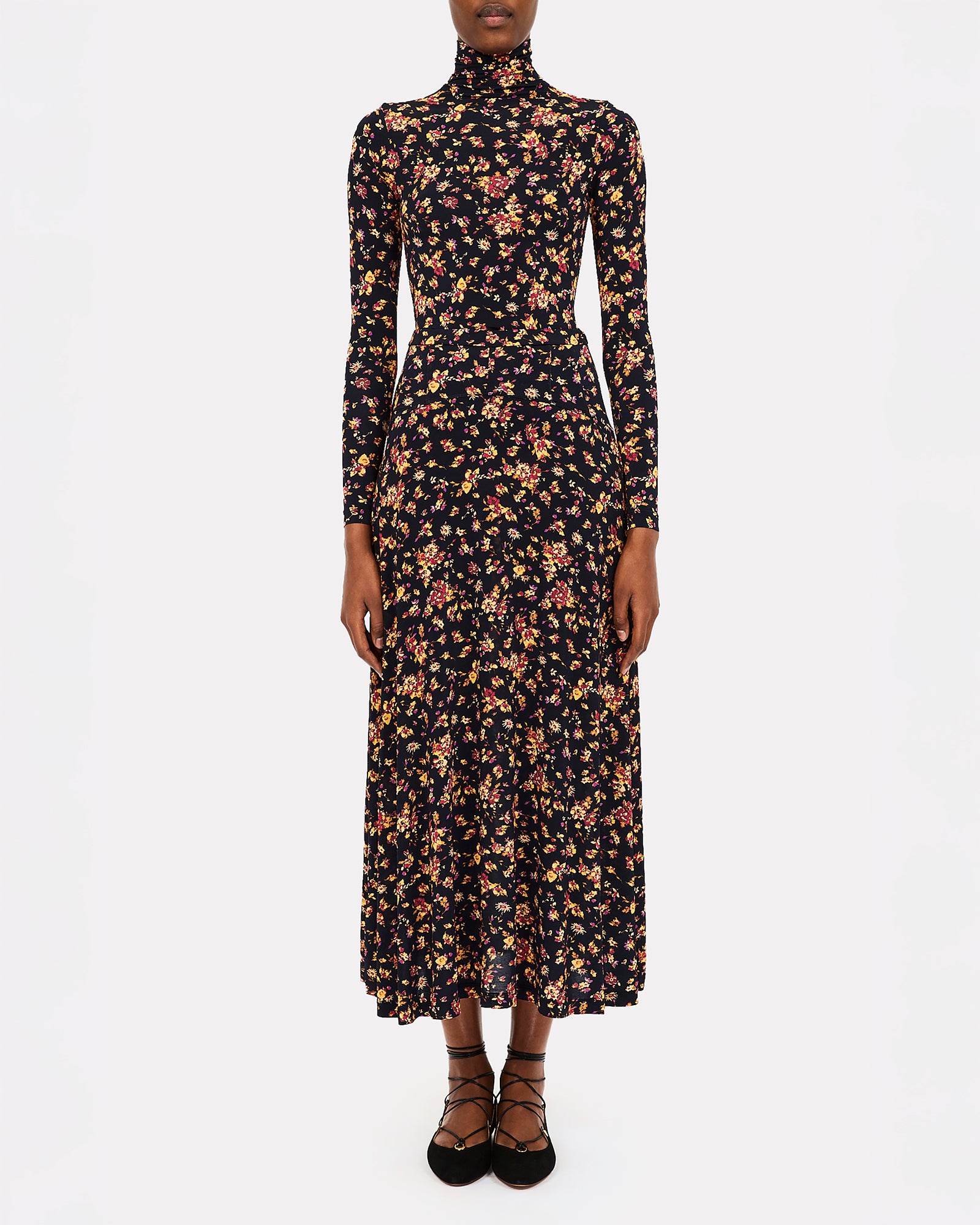 A model wearing a long-sleeved, high-neck midi dress with an all-over dense floral print on a black background, paired with black lace-up platform sandals, against a plain white studio background.