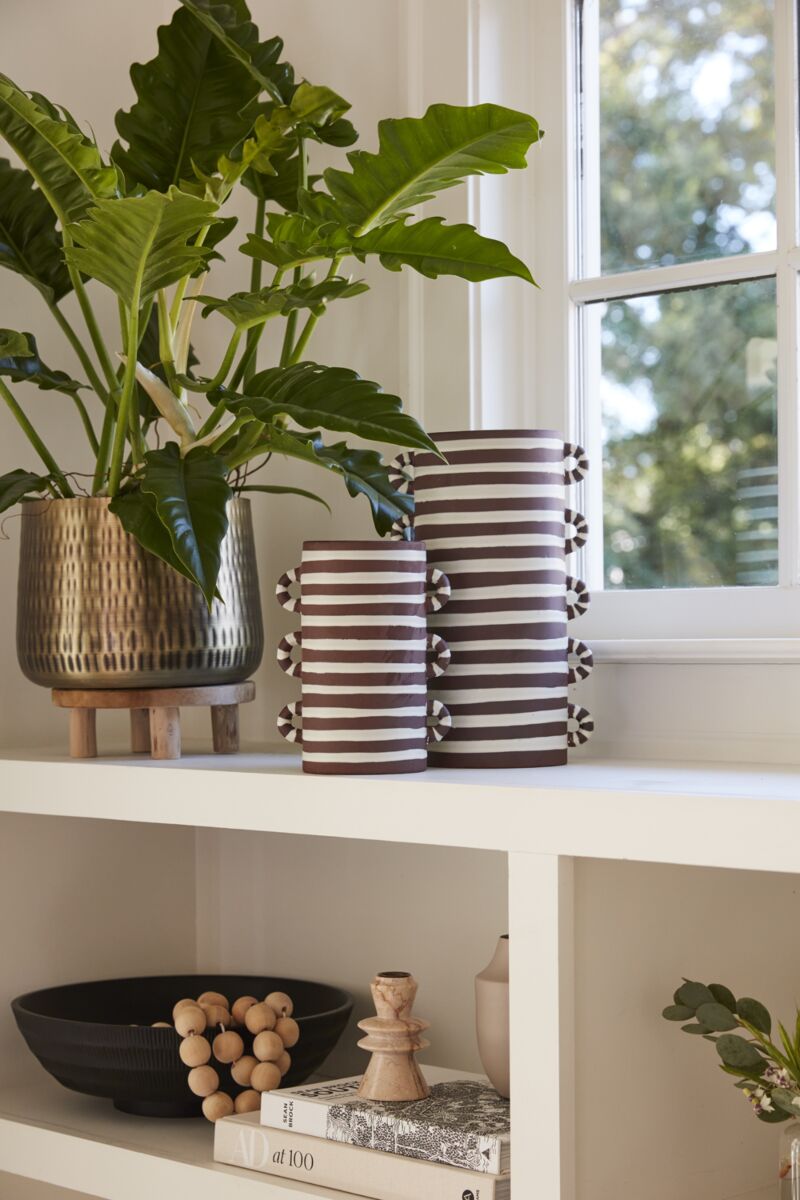 Decorative shelf with striped vases, a plant, and other items against a window backdrop.
