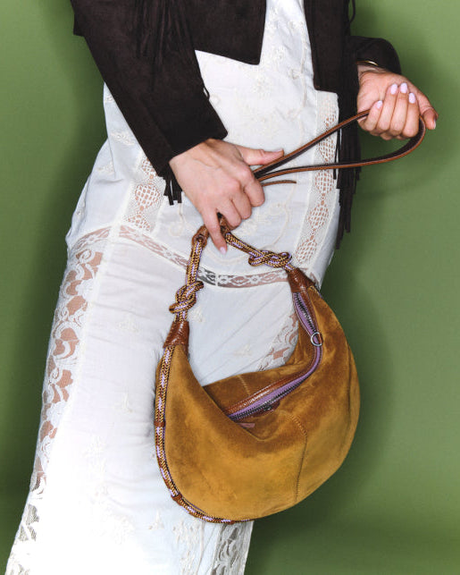 Person holding a brown suede handbag against a green background