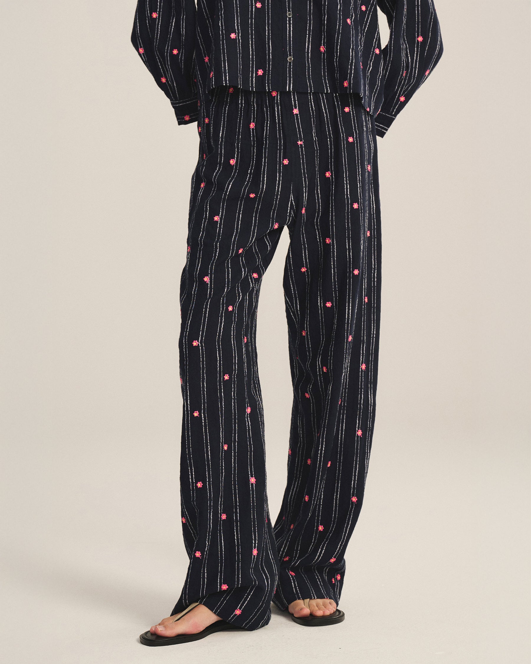 Black pant and top set with white striped and pink flower embroidery detailing on a beige background