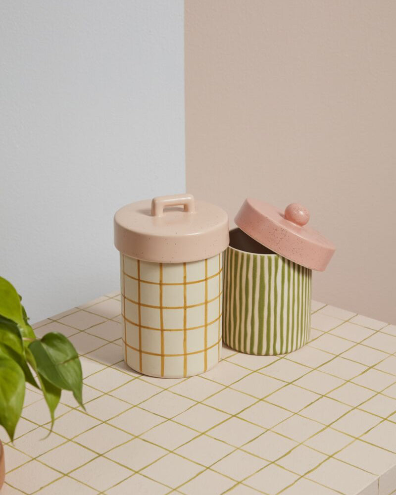 Two cylindrical storage containers with pink lids on a tiled surface.
