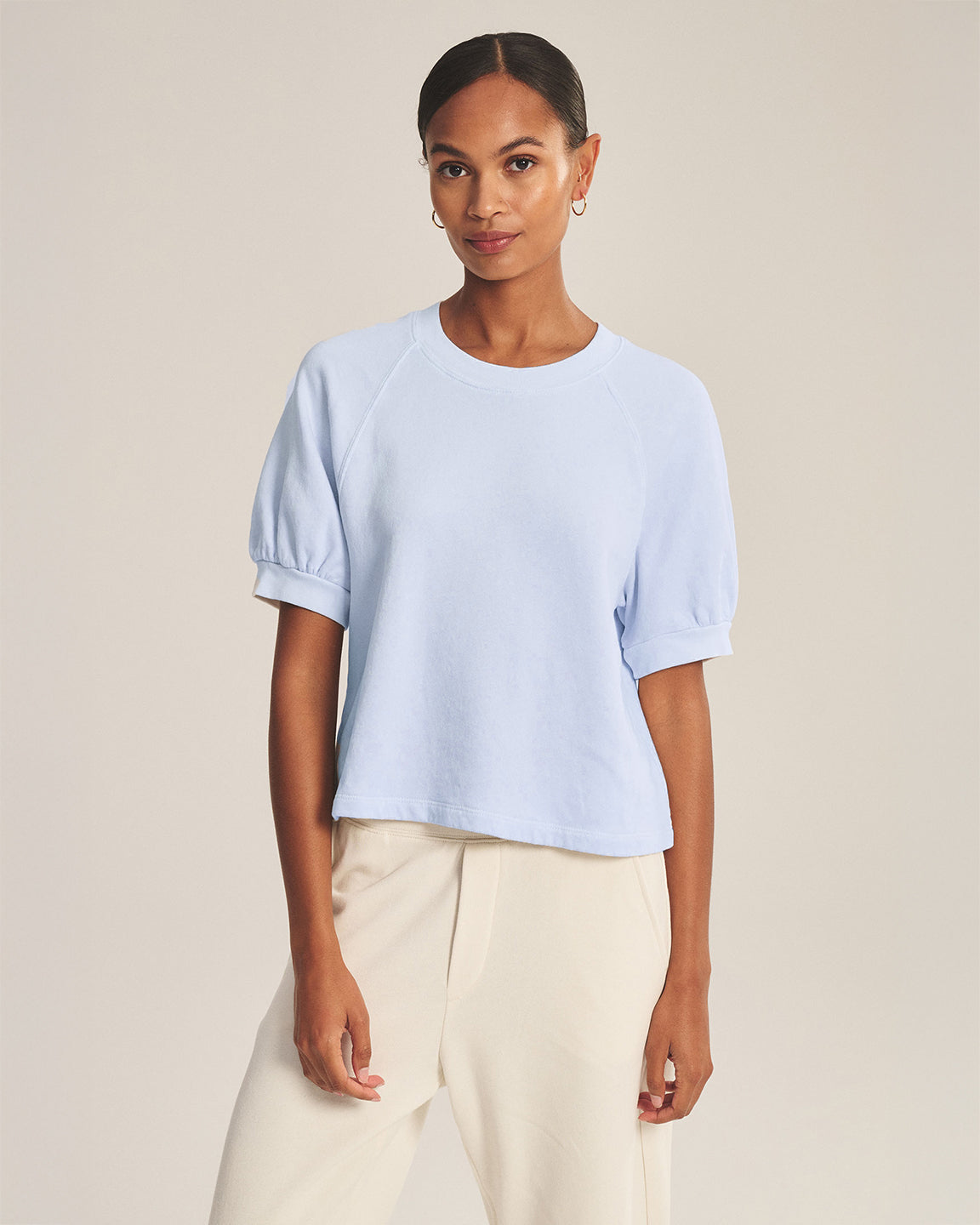 Woman wearing a light blue top and white pants on a beige background