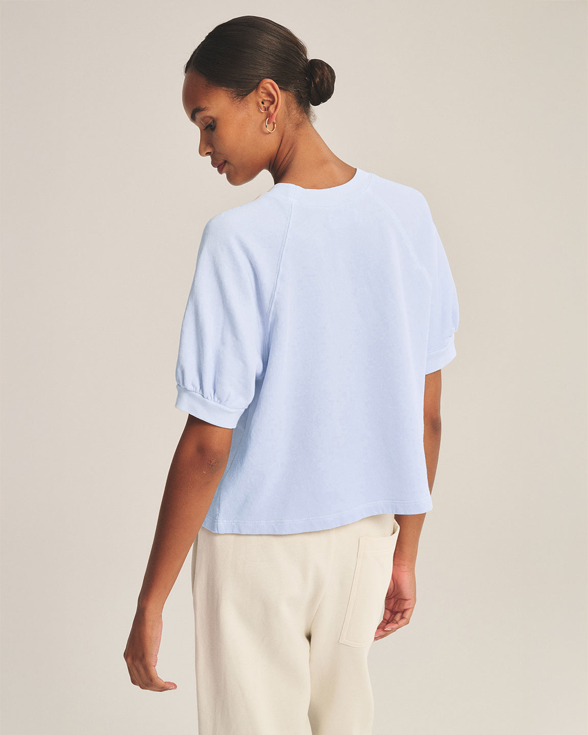 Woman wearing a light blue top and beige pants against a plain background