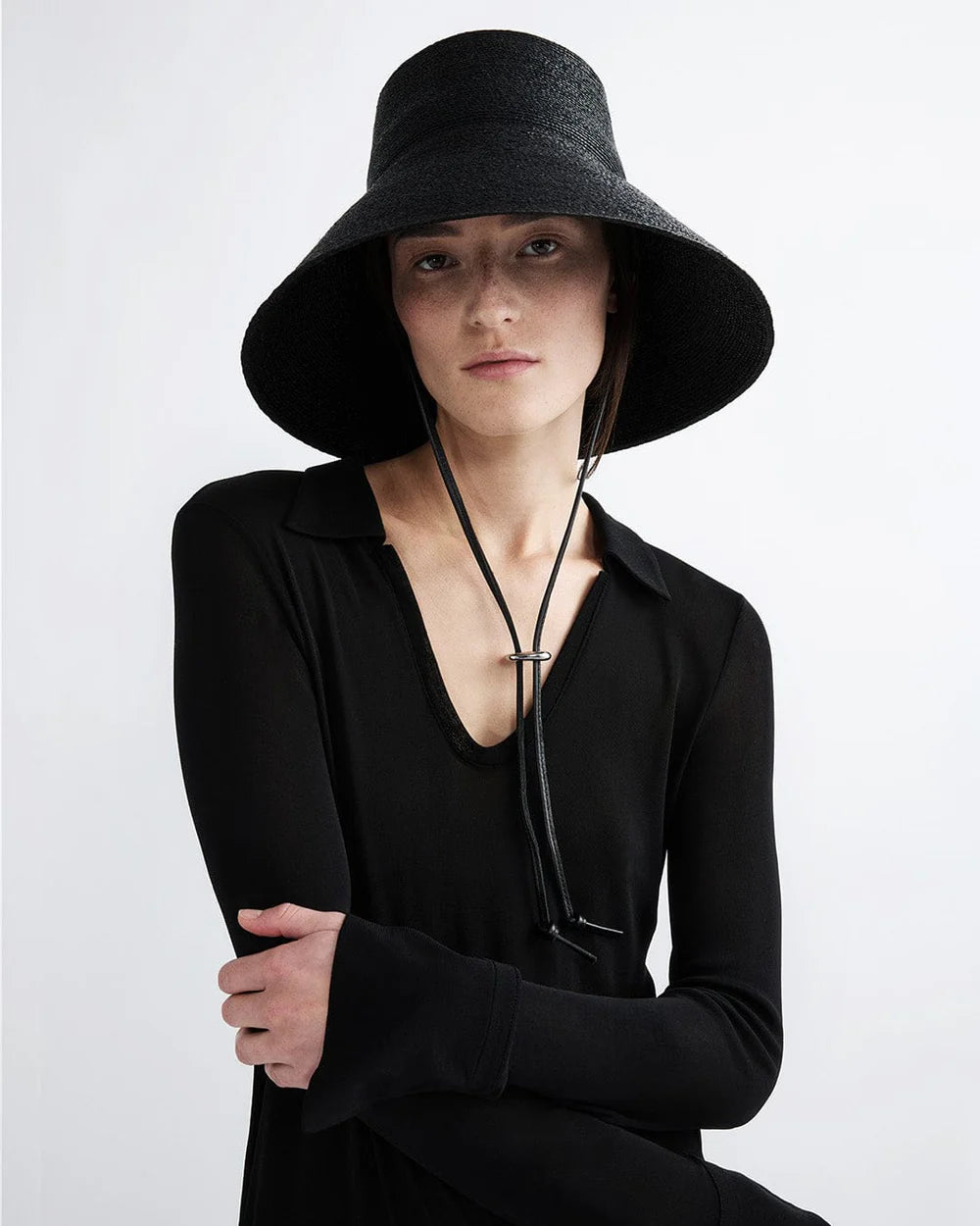 Person wearing a black wide-brimmed hat and black outfit on a white background