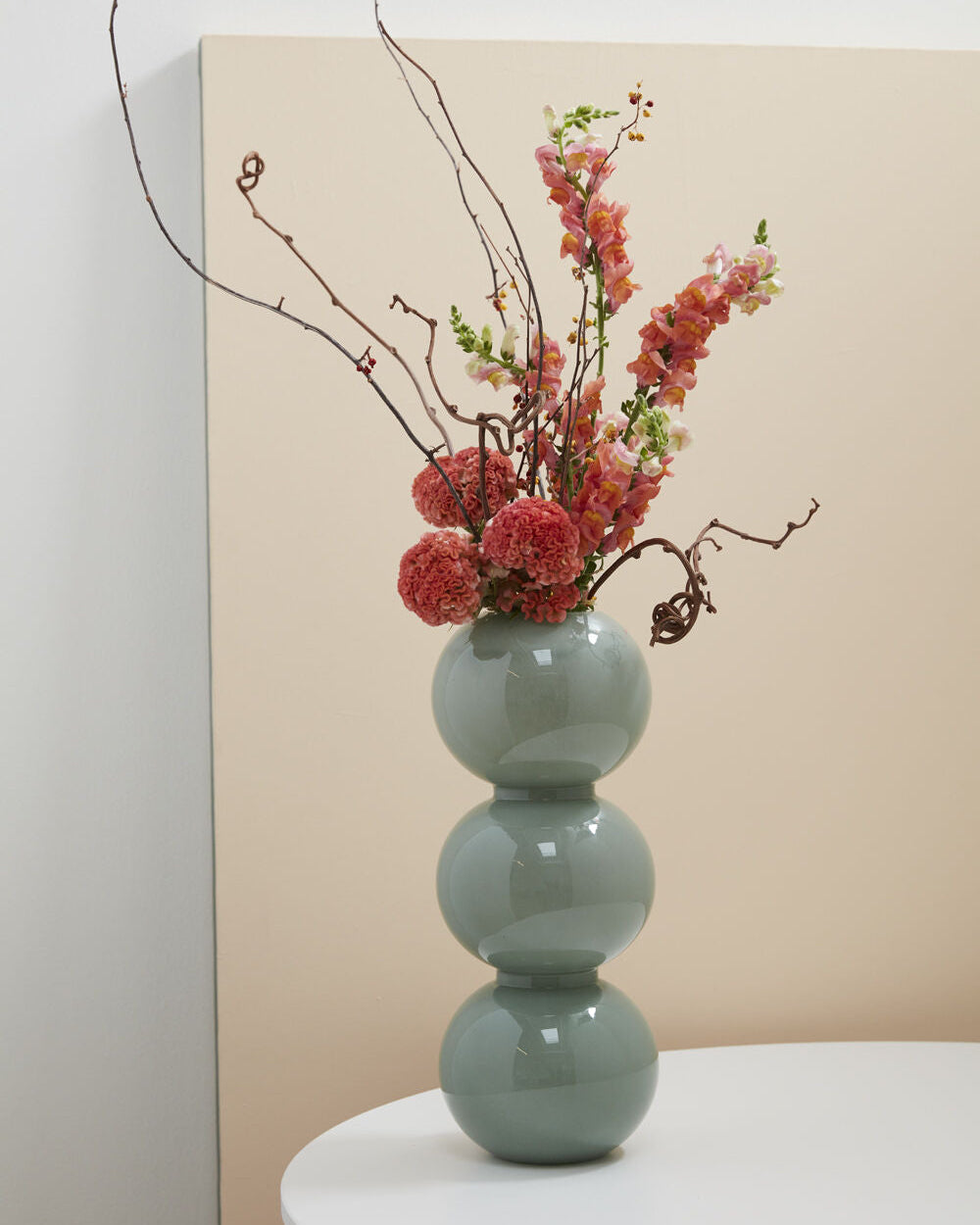 Decorative vase with flowers on a white surface against a beige wall
