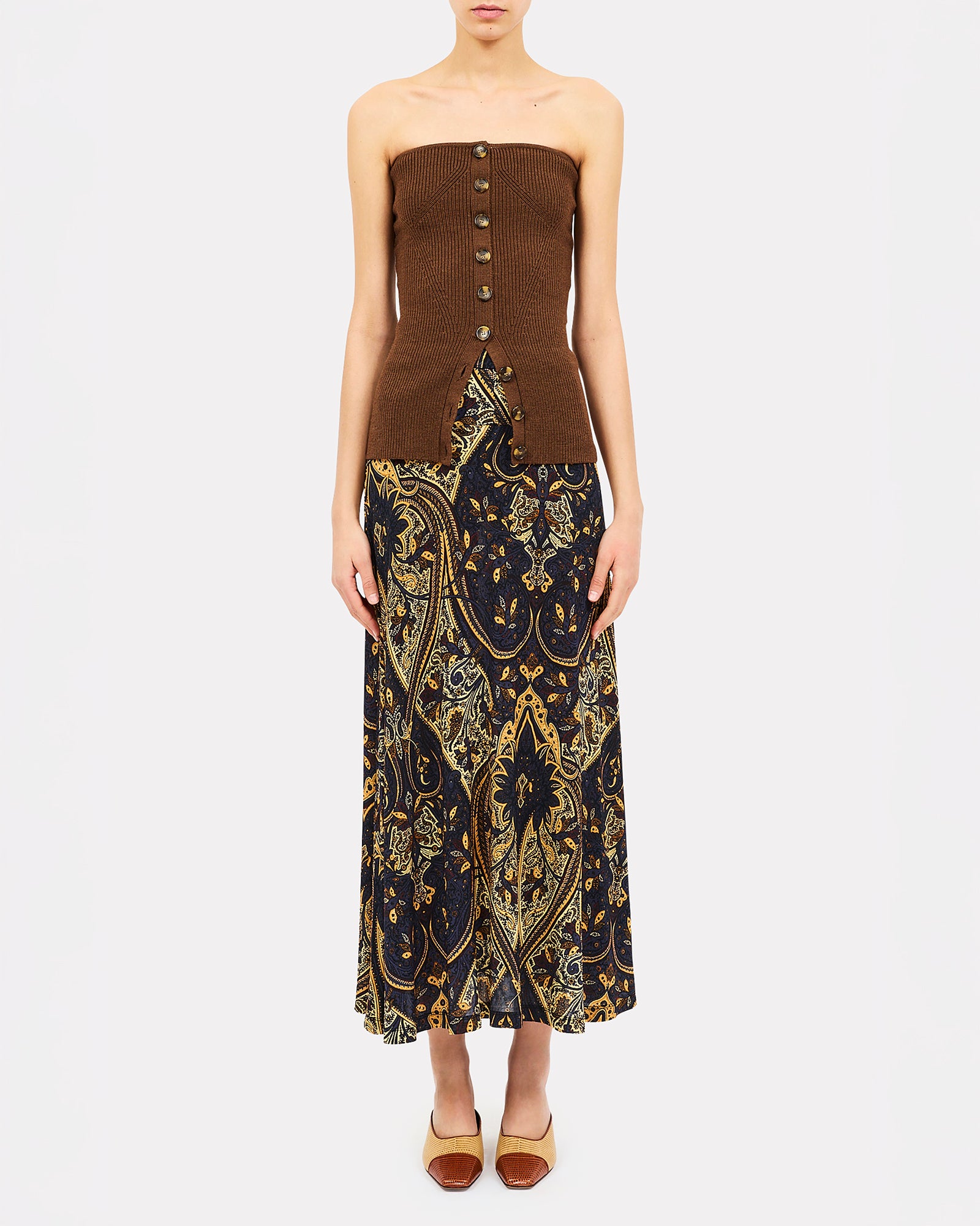 A model wearing a strapless tube top and maxi skirt set. The top is a solid medium brown with a button-down front, and the skirt features a dark navy blue and gold paisley pattern.