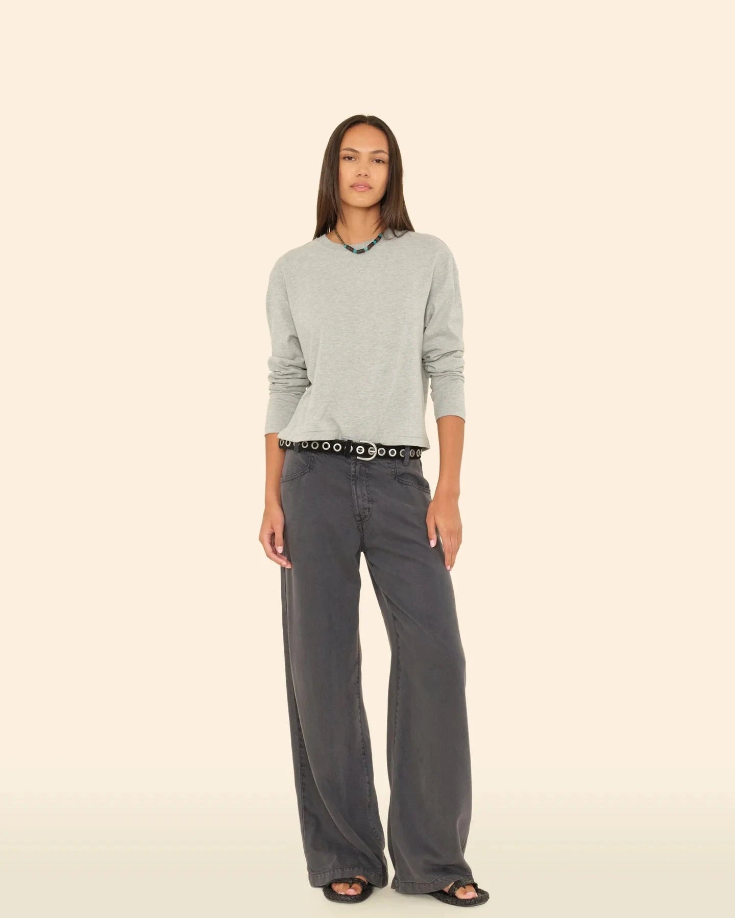 Woman wearing a light gray sweater and dark gray wide-leg pants on a beige background