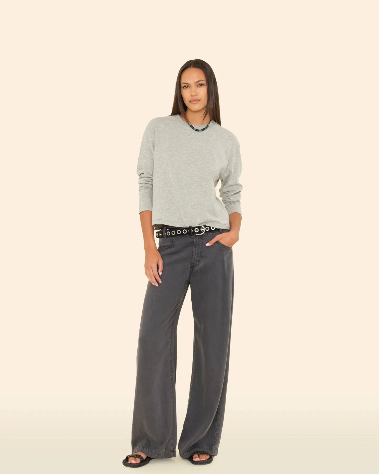 Woman wearing a gray sweater and wide-leg pants on a beige background