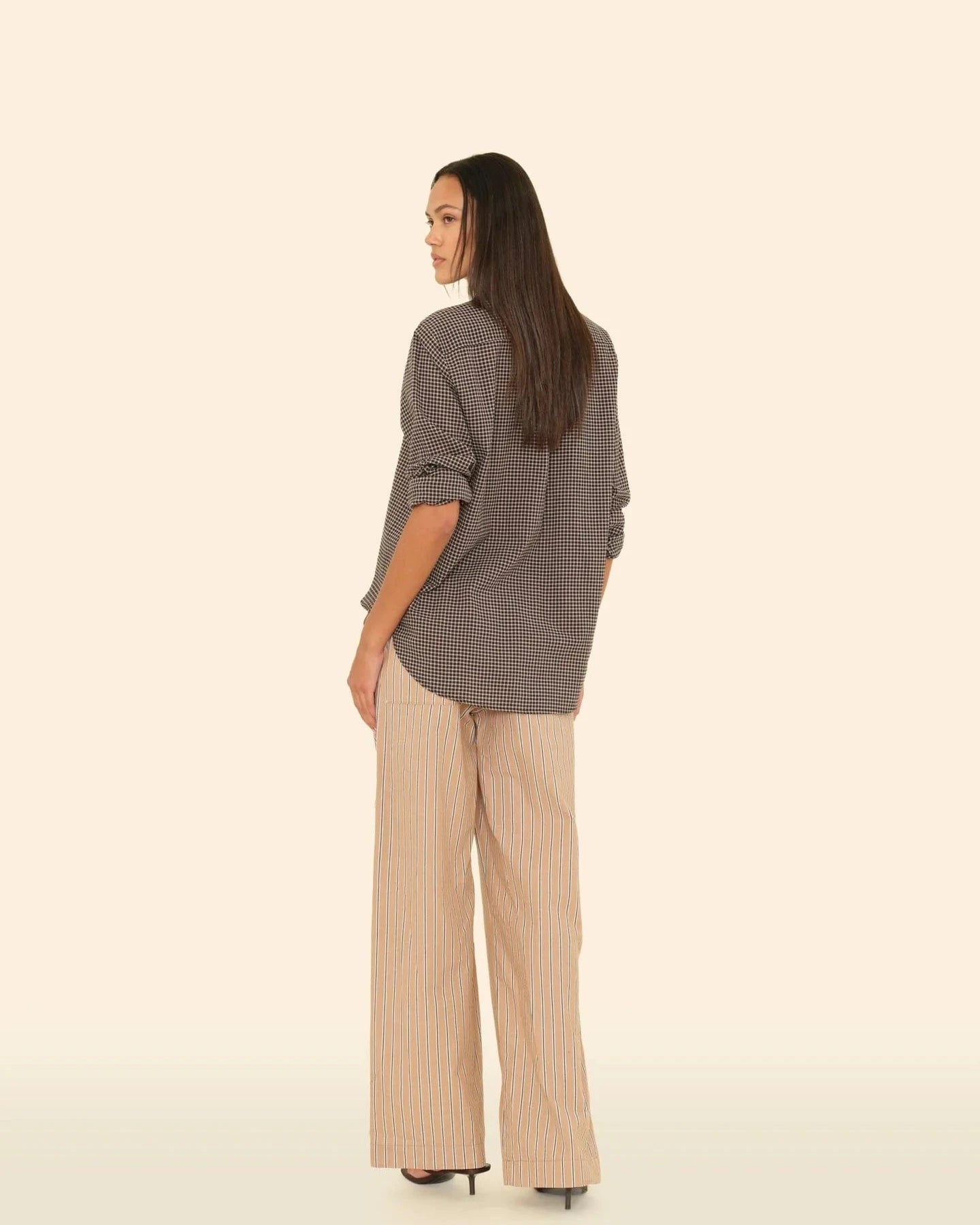 Woman wearing a gray checkered shirt and beige pants on a beige background